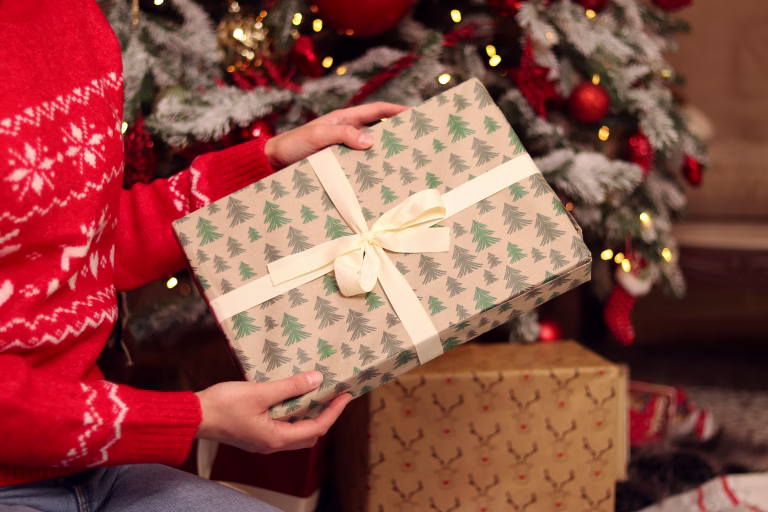 Close-up of New Year's gift with a bow in hands. Gift in a box with festive packaging and a bow. Christmas or New Year. To take or to put a gift. Surprise. Girl examines a box in a gift wrapping