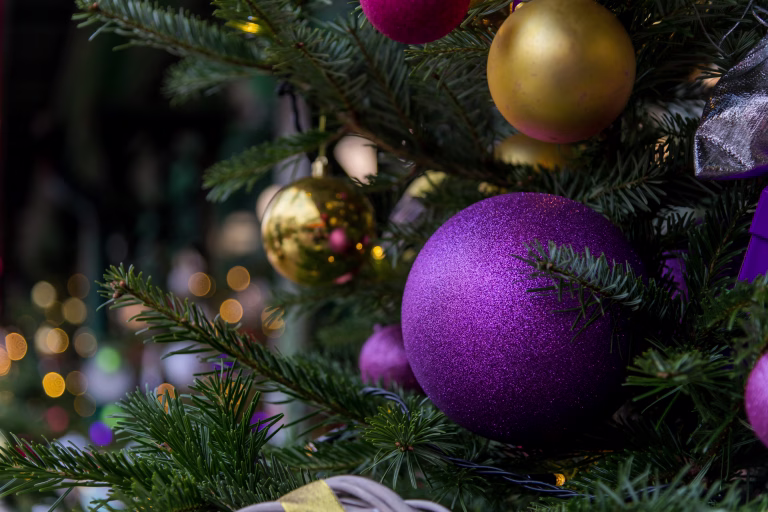 Colorful ornaments hang from a well-decorated evergreen tree along a bustling street. The warm glow of lights creates a cheerful atmosphere, inviting passersby to enjoy the holiday spirit.
