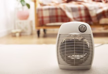 Tega z električnim grelnikom nikoli ne počnite! Posledice so lahko drage, še posebej v tem prostoru Fan heater on the floor in living room with sofa at background