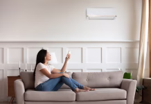 Na kaj morate biti pozorni pri izbiri klimatske naprave Vietnamese young woman relaxing on comfy couch in contemporary living room with air conditioner, holding remote control turning on or off cooler system, setting comfortable temperature at modern home