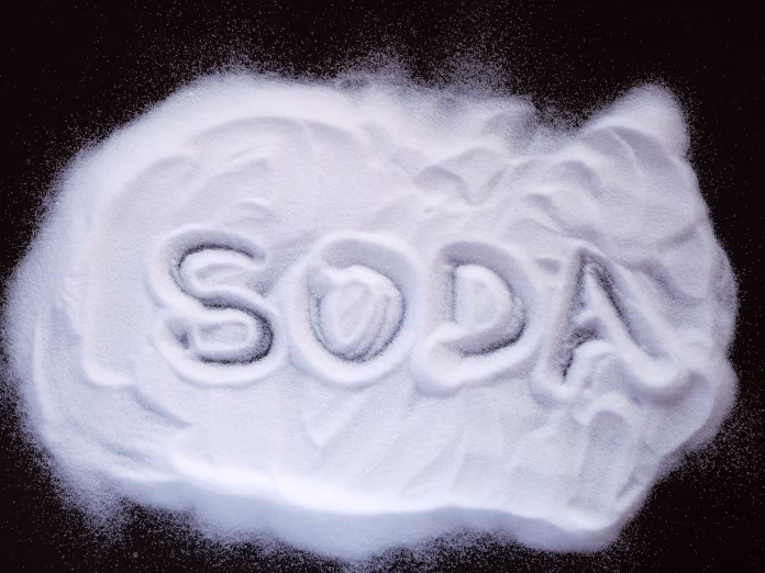 White powder sprinkled on a dark surface with the letters "Soda" painted on it. View from above.