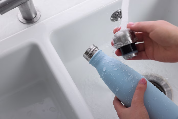 Woman washing thermo bottle in kitchen, above view