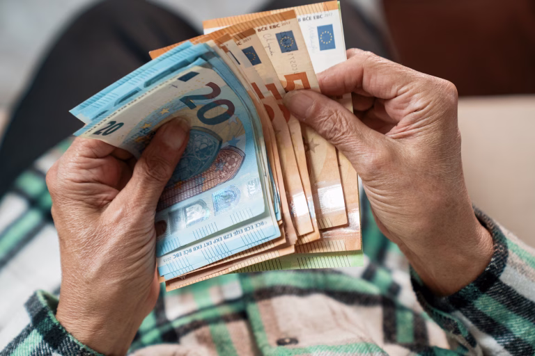 A bundle of euros in the hands of an elderly pensioner. The concept of financial security in old age.
