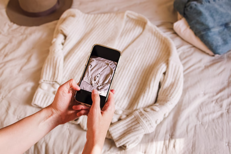 Close-up of woman's hands taking picture of her used sweater. Selling used clothes online, reuse, sustainable consumption