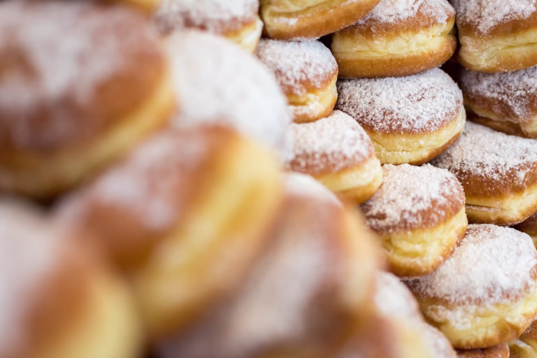 Donuts with no holes, a traditional deep fried dough sprinkled with powdered sugar, filled with marmalade and stacked for display. Photographed with shallow depth of field and more donuts in the foreground.