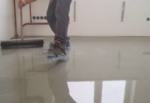 Kdaj je pohoden estrih? Finishing works - Needle roller for bulk floor. A worker rolls out the liquid floor with a trowel. Squeegee for distributing the mixture. The worker levels the liquid floor.