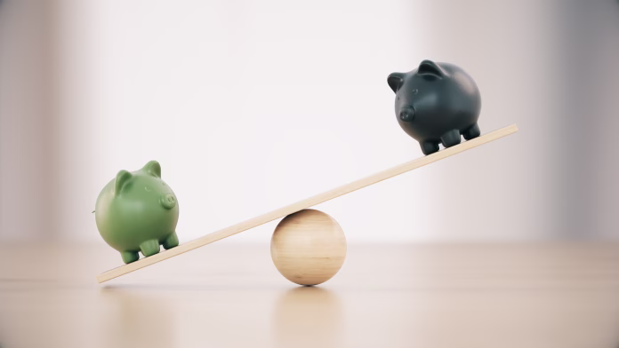 Green And Black Ceramic Piggy Banks On A Seesaw Before Defocused Wooden Background