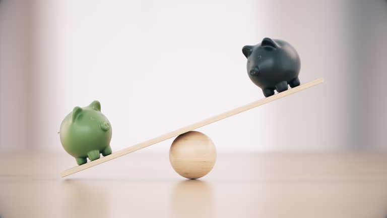 Green And Black Ceramic Piggy Banks On A Seesaw Before Defocused Wooden Background