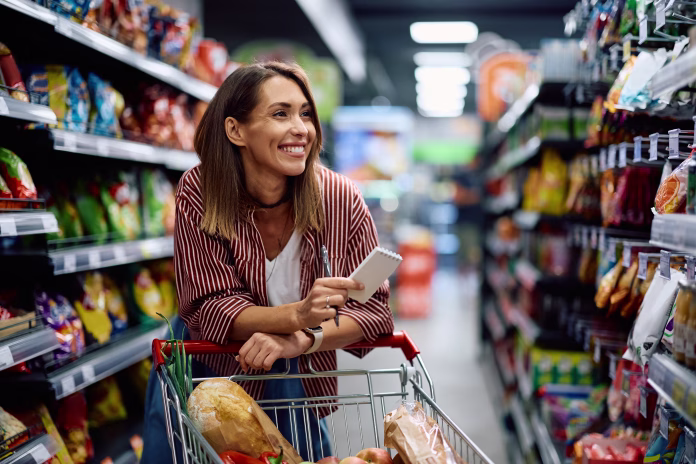 Happy woman using grocery list while shopping at supermarket.