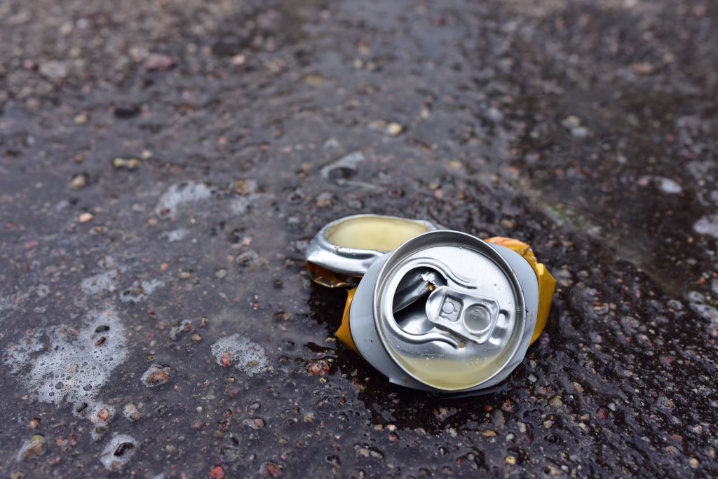 Crumpled a beer can on asphalt with spilled alcohol. Discarded broken carbonated drink can at a road. Problem social, crime. Environmental pollution, waste, ecology. Crushed juce. Out of focus