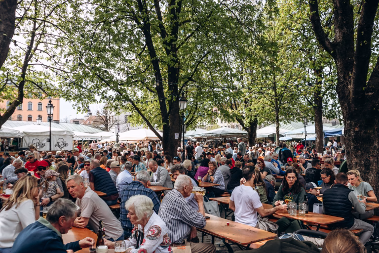 Munich, Germany - April 15, 2025: Crowds of locals and tourists enjoying food and drinks at outdoor beer garden tables at Viktualienmarkt in the historic center of Munich, Bavaria, Germany