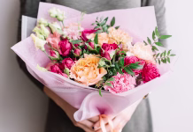 Rože, ki jih nikakor ne podarjajte za 8. marec: mnogi naredijo to napako, prinašajo pa nesrečo in žalost Very nice young woman holding a colourful fresh blossoming flower bouquet of different sorts of roses, carnations, eustoma, peonies on the grey wall background
