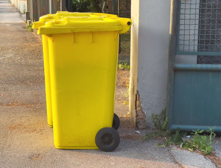 Yellow trash bins on street in sunlight near fenced area, lifestyle