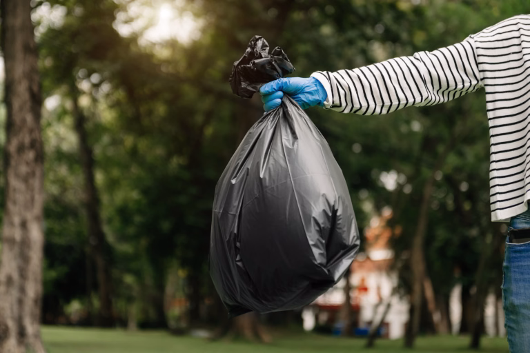 Hand holding garbage black bag putting in to trash to clean. Clearing, pollution, ecology and plastic concept.