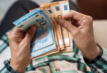 Novica za upokojence: Višje pokojnine že maja! Poglejte, koliko več boste dobili … A bundle of euros in the hands of an elderly pensioner. The concept of financial security in old age.