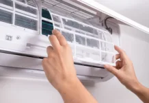 Ne prižigajte klime, dokler ne naredite tega: 2-minutni trik odpravi smrad in bakterije ter zniža račune Close up of man inserting new filter into air conditioner unit during regular maintenance. Concept of HVAC service, home care, clean indoor air, and energy-efficient cooling.