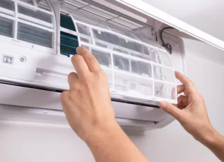 Ne prižigajte klime, dokler ne naredite tega: 2-minutni trik odpravi smrad in bakterije ter zniža račune Close up of man inserting new filter into air conditioner unit during regular maintenance. Concept of HVAC service, home care, clean indoor air, and energy-efficient cooling.