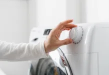 Prepolovite račun za elektriko! Najdražja napaka pri pranju perila in program, ki vam prihrani denar cropped shot of woman hand turn on automatic washing machine or select program with knob on control panel in white bathroom, modern appliances at home