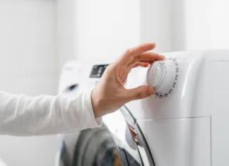 Prepolovite račun za elektriko! Najdražja napaka pri pranju perila in program, ki vam prihrani denar cropped shot of woman hand turn on automatic washing machine or select program with knob on control panel in white bathroom, modern appliances at home