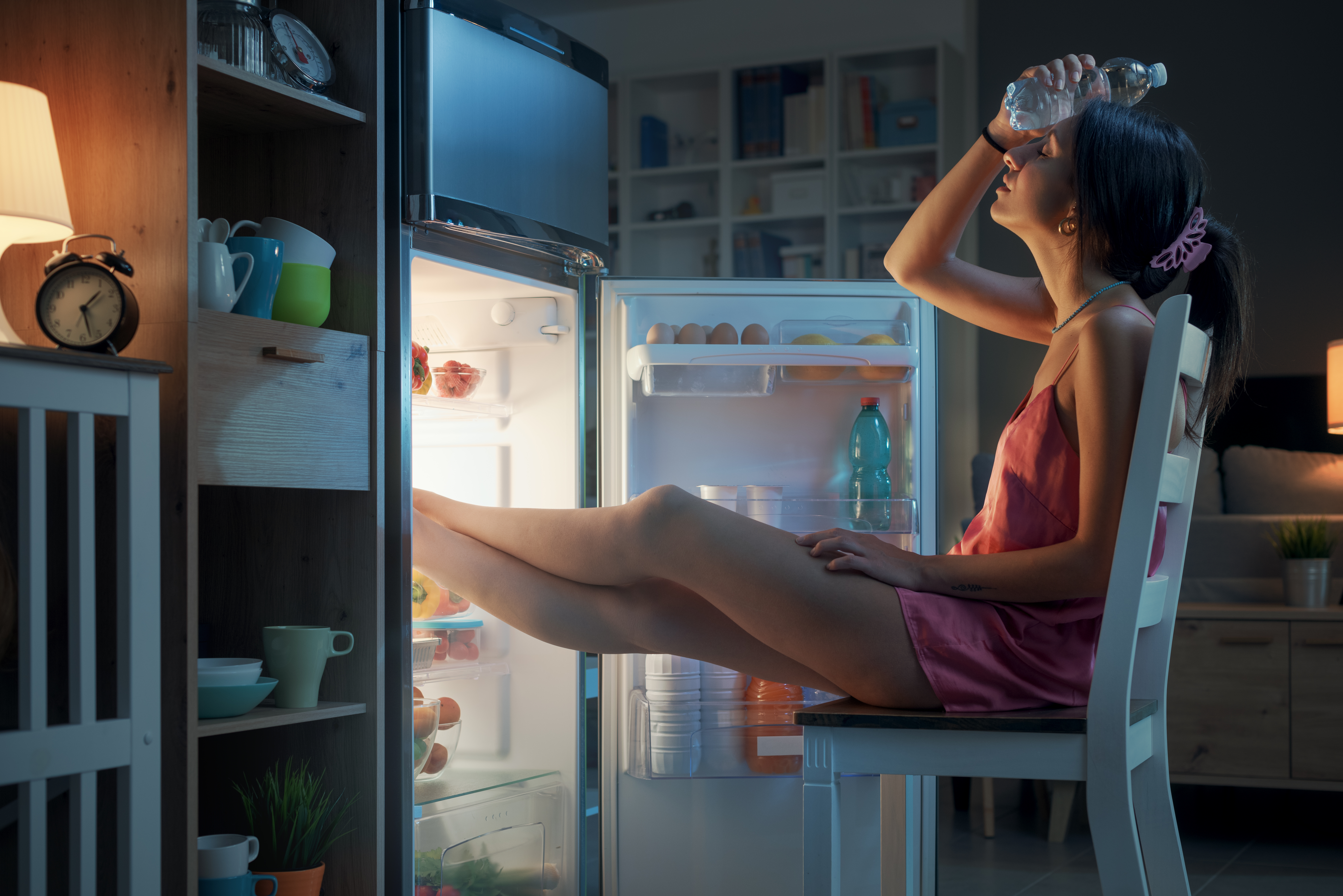 woman-suffering-from-the-heat-in-summer-she-is-resting-with-her-feet-in-the-fridge-and-holding-a-water-bottle-stockpack-istock Ženska trpi zaradi poletne vročine; počiva z nogami v hladilniku in v roki drži steklenico vode.