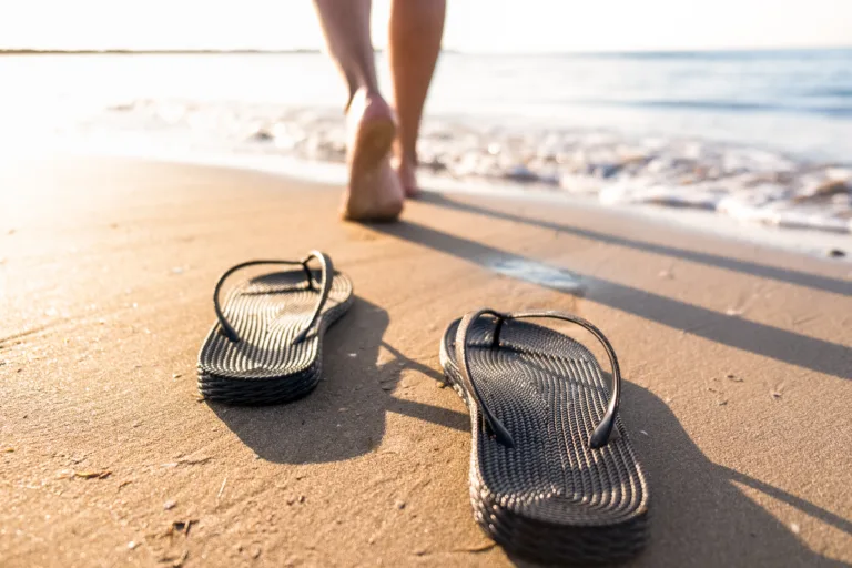 Woman's legs move away from their sandals towards the sea water on a beach