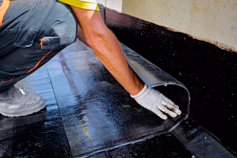 Worker in gloves prepare for melting, manually place and unroll rolled up, sheet of waterproofing installation over concrete. Residential building under construction placing water insulation