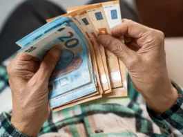 Znano je, koliko bo znašala božičnica 2026: kdo dobi celoten znesek in kdo manj? A bundle of euros in the hands of an elderly pensioner. The concept of financial security in old age.