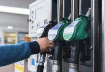 To so nove cene goriv: nekateri z njimi ne bodo zadovoljni A customer interacts with fuel pumps at a gas station, engaging in refueling their vehicle while surrounding areas are busy and well-maintained during daylight.