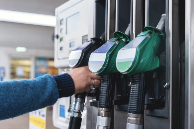 A customer interacts with fuel pumps at a gas station, engaging in refueling their vehicle while surrounding areas are busy and well-maintained during daylight.