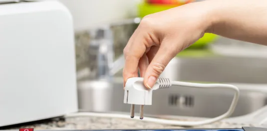 Close up of a woman's hand plugging a toaster into the electrical outlet in a socket on a kitchen counter at home