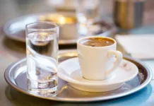 Ali veste, zakaj v kavarni ob kavi dobite kozarec vode? Ni namenjena pitju, kot mislijo mnogi Cup of coffee and glass of water on cafe table