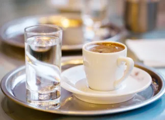 Ali veste, zakaj v kavarni ob kavi dobite kozarec vode? Ni namenjena pitju, kot mislijo mnogi Cup of coffee and glass of water on cafe table
