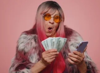 Tri stvari na mizi privlačijo bogastvo: babičin trik, zaradi katerega ne boste vedeli, kam z denarjem Happy tourist woman looking smartphone display sincerely rejoicing win, receiving money dollar cash banknotes, success lottery luck. Senior stylish grandmother isolated alone on blue studio background