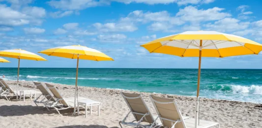 Luxury beach chairs and yellow umbrellas on white sand at the sea in Fort Lauderdale, Florida. No people.