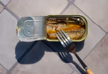 Čim prej jo odstranite iz gospodinjstva! EU prepoveduje kemikalijo, ki jo povezujejo z rakom, sladkorno boleznijo in neplodnostjo Overhead view of open sardine tin with a fork inside, casting long shadows on a tiled surface. Simple food or emergency meal.