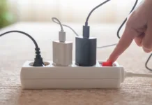 Ta naprava porabi več elektrike kot klimatska naprava, izklopi pa jo le malokdo: to najbolj vpliva na račun za elektriko Person pressing red on/off switch on white power strip to cut electricity to multiple chargers, symbolizing mindful power use, energy saving, lower bills and household sustainability