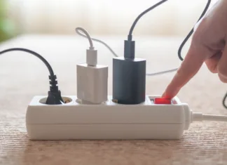 Ta naprava porabi več elektrike kot klimatska naprava, izklopi pa jo le malokdo: to najbolj vpliva na račun za elektriko Person pressing red on/off switch on white power strip to cut electricity to multiple chargers, symbolizing mindful power use, energy saving, lower bills and household sustainability