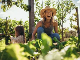 Beautiful young female farmer working in her garden with her daughter sitting by. Young mother and daughter working in the farm.