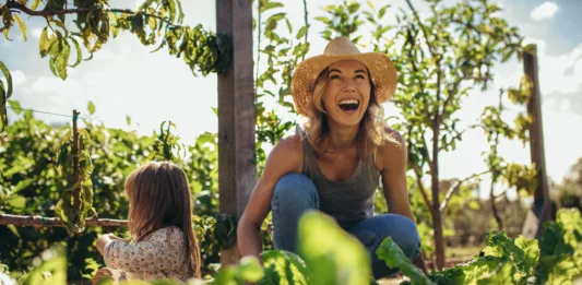 Beautiful young female farmer working in her garden with her daughter sitting by. Young mother and daughter working in the farm.