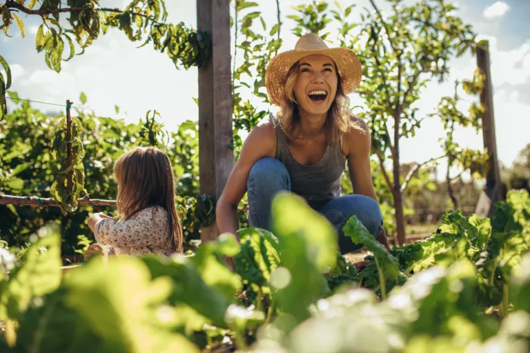 Beautiful young female farmer working in her garden with her daughter sitting by. Young mother and daughter working in the farm.