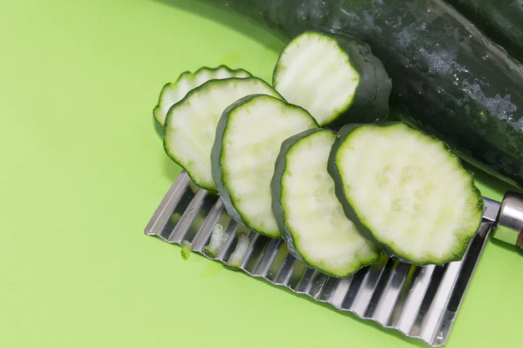 Chopped cucamber ordered on top of the vegetable chopper on green background
