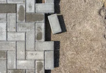 Kdaj je najboljše polagati tlakovce? Laying gray concrete paving slabs in a house walkway. Process of construction of brick paved sidewalk, half built pavement road.