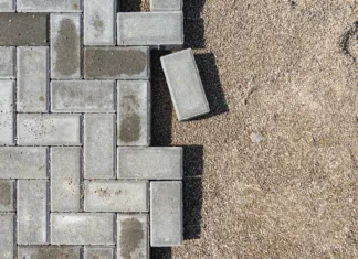 Kdaj je najboljše polagati tlakovce? Laying gray concrete paving slabs in a house walkway. Process of construction of brick paved sidewalk, half built pavement road.