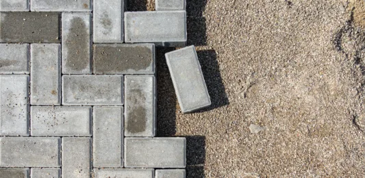 Laying gray concrete paving slabs in a house walkway. Process of construction of brick paved sidewalk, half built pavement road.