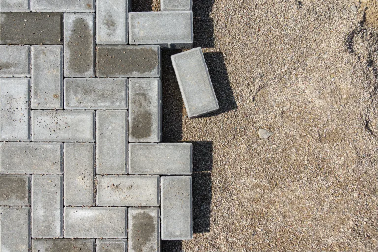 Laying gray concrete paving slabs in a house walkway. Process of construction of brick paved sidewalk, half built pavement road.