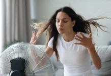 Strokovnjaki opozarjajo: ventilatorja nikar ne uporabljajte, ko temperature presežejo to mejo Millennial Caucasian girl sit on sofa in living room breathe fresh air from floor ventilator suffer from summer heat at home, young woman feel hot use fan at home struggle with lack of air condition