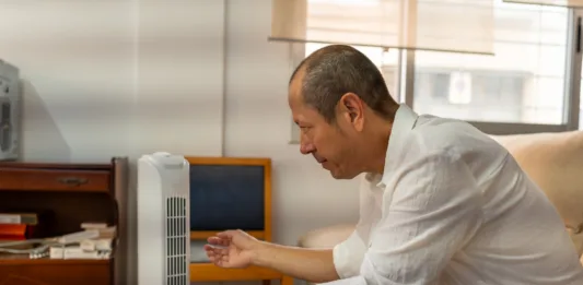 Relaxed male feeling relief from portable air conditioner cooling in warm home interior during sweltering summer afternoon