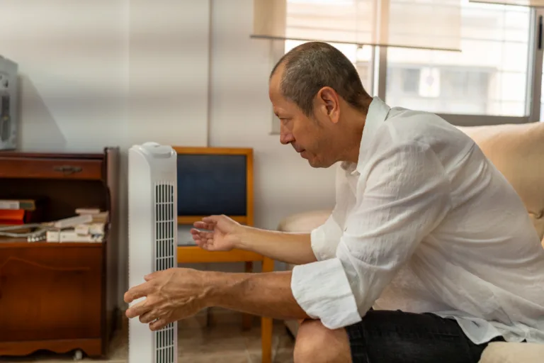 Relaxed male feeling relief from portable air conditioner cooling in warm home interior during sweltering summer afternoon