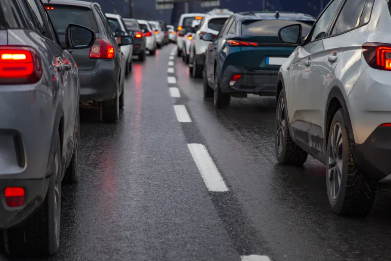 Traffic jam with a row of cars on a highway during rush hour in the evening after work. red brake lights of stopped cars on the background of wet asphalt with white lanes at sunset