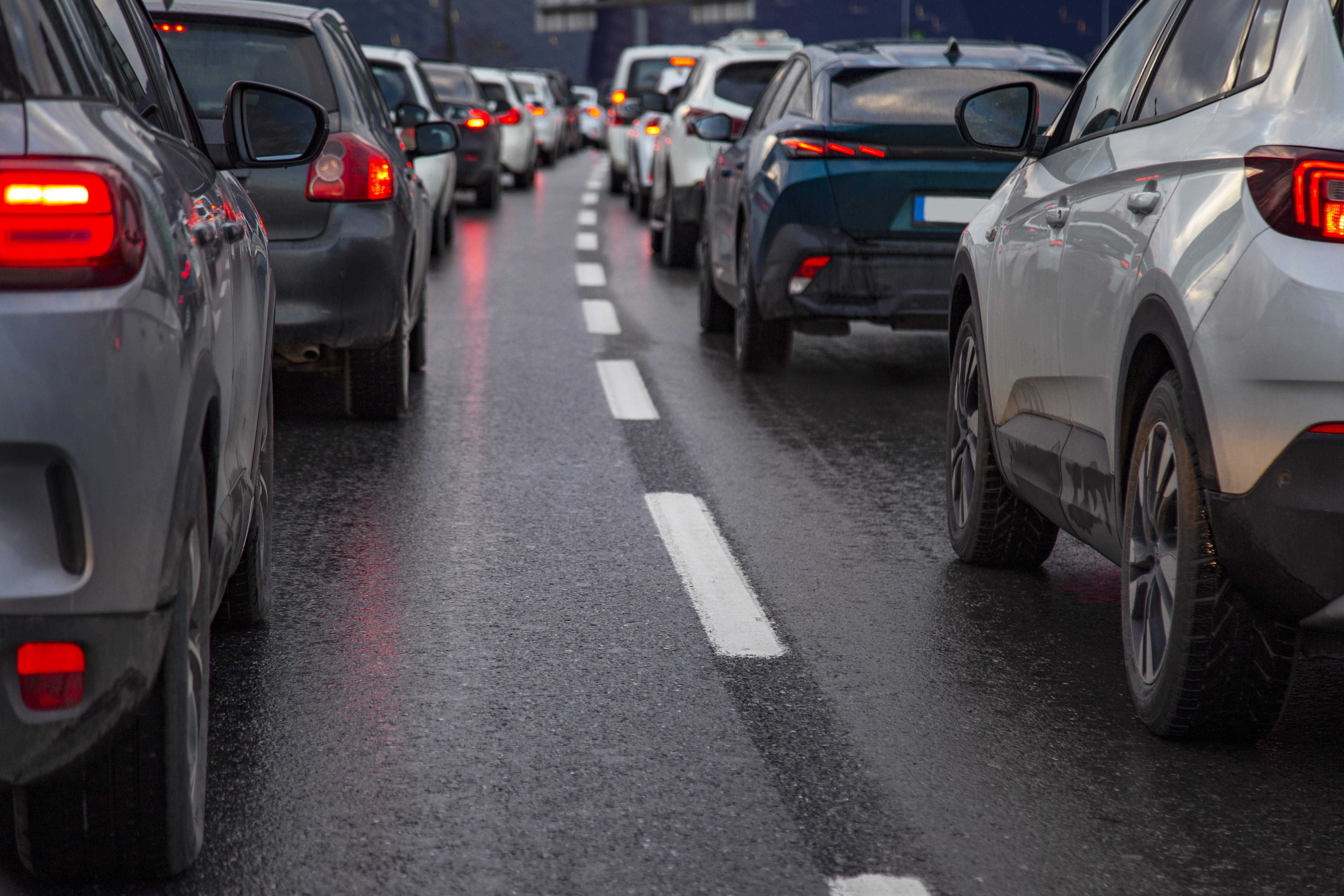 Velika sprememba za voznike v EU v veljavi od torka: prinašamo podrobnosti novih pravil … Traffic jam with a row of cars on a highway during rush hour in the evening after work. red brake lights of stopped cars on the background of wet asphalt with white lanes at sunset